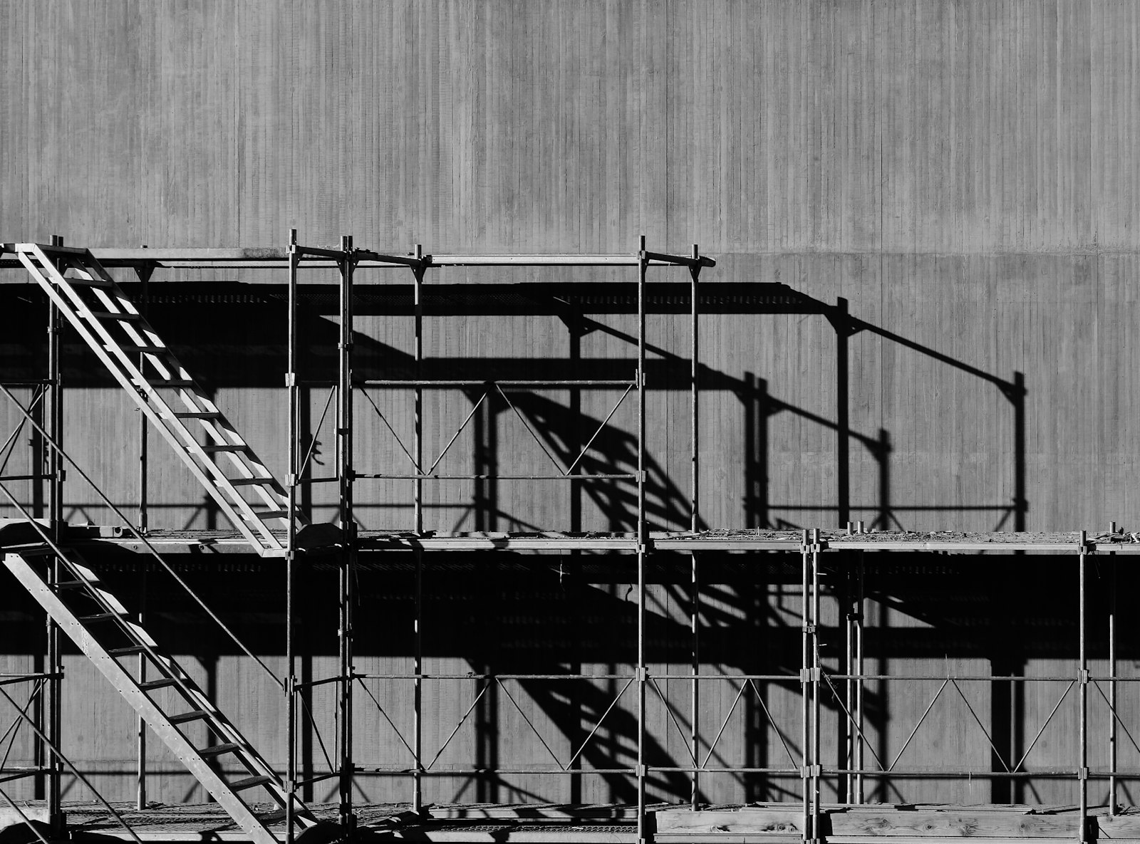 Steel scaffolding and stairs casting shadows on a concrete wall